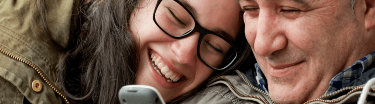 happy dad and daughter lookig at her phone